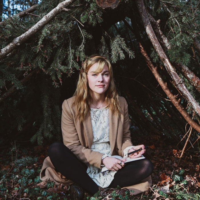 Oregon-based author and artist, Caroline Holm stitting under a tree in the wilds of Oregon