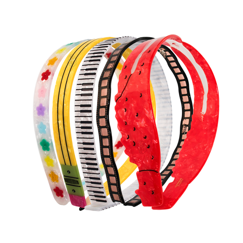 A set of six translucent plastic headbands with various printed patterns, including piano keys, film reels, stars, and stripes, arranged on a solid white background.